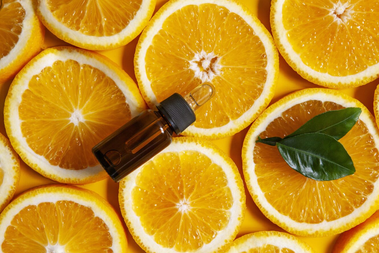 sliced oranges in background with essential oil in foreground