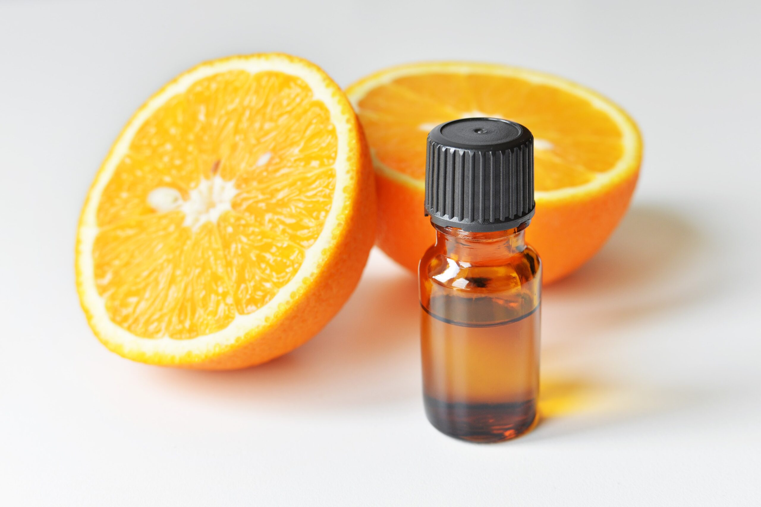 oranges in background with dark essential oil bottle