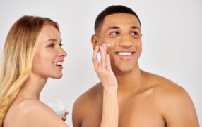 Couple smiling together woman applies skincare to parter