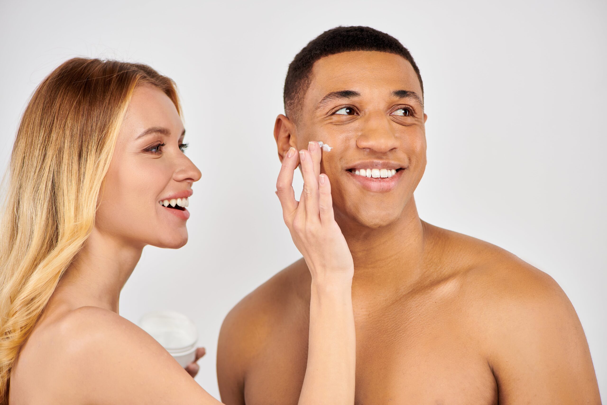 Couple smiling together woman applies skincare to parter