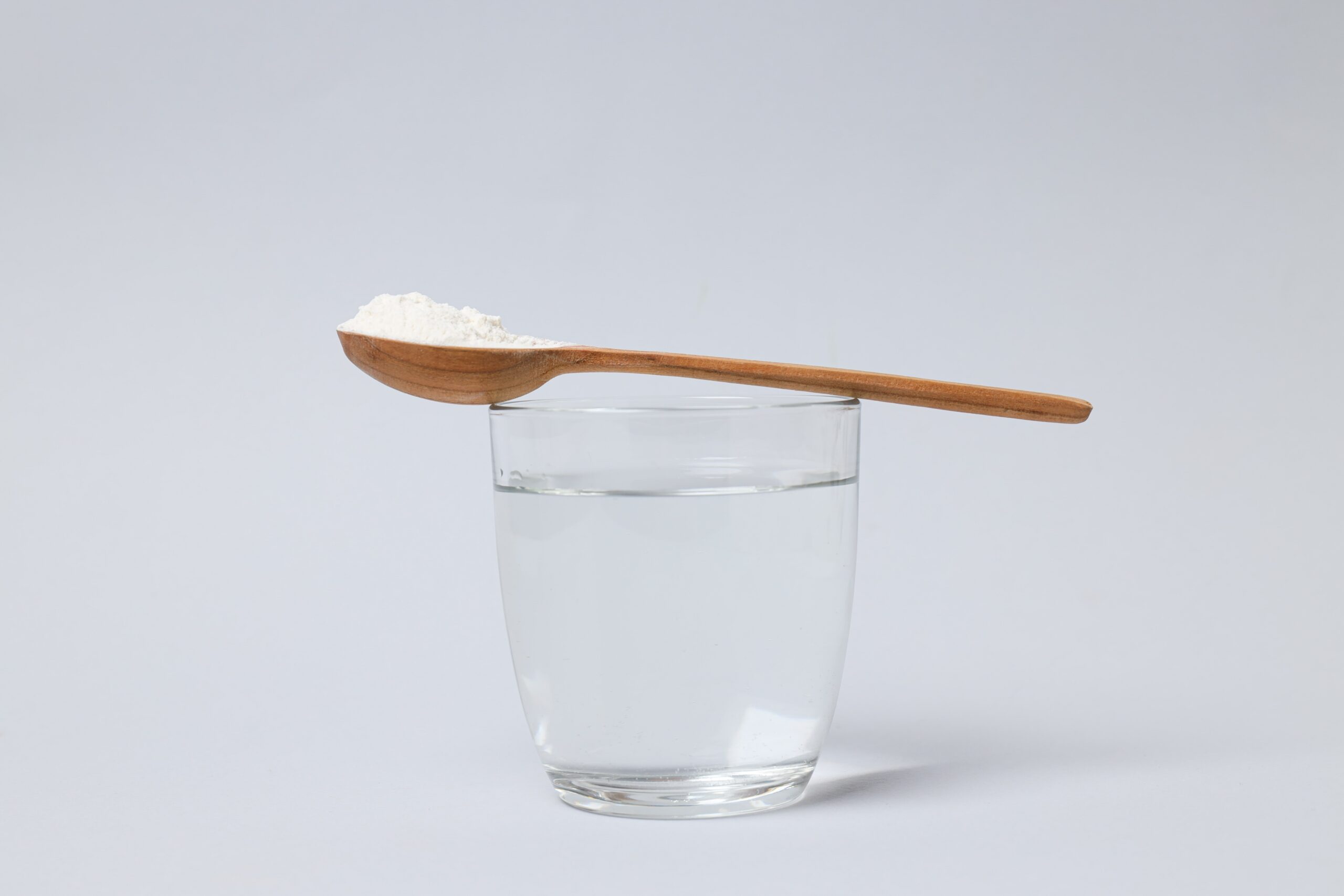 Collagen powder scooped in wooden spoon resting on glass of water