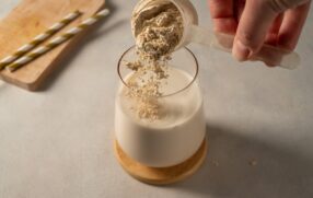 Pouring collagen powder into drink using plastic scoop.