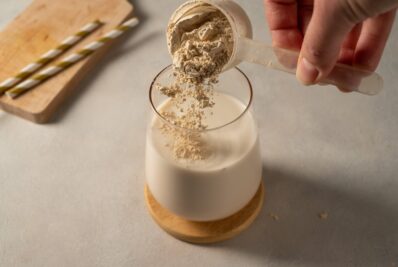 Pouring collagen powder into drink using plastic scoop.