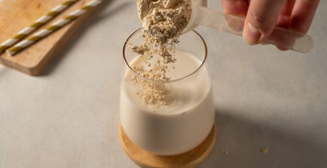 Pouring collagen powder into drink using plastic scoop.