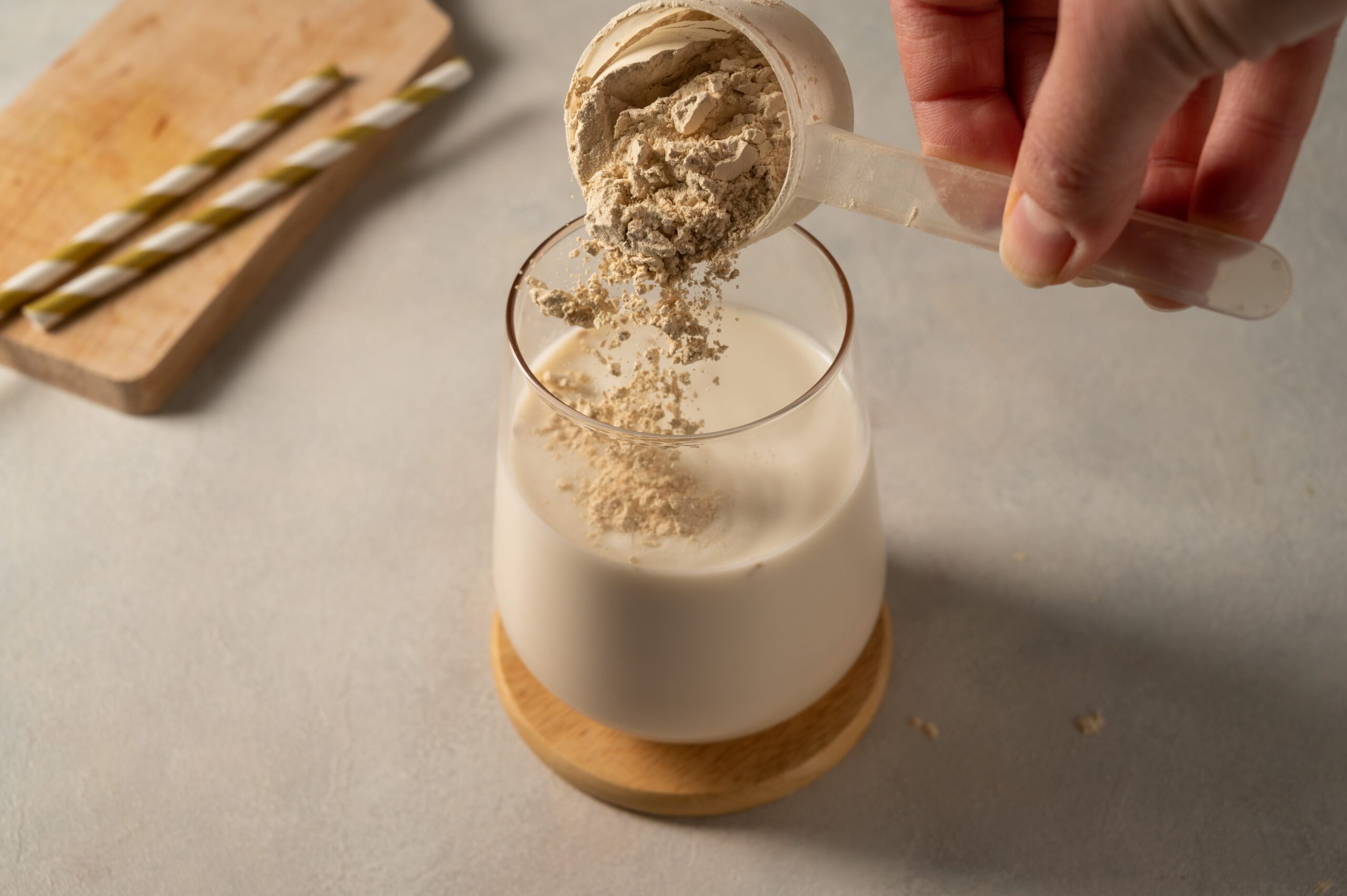 Pouring collagen powder into drink using plastic scoop.